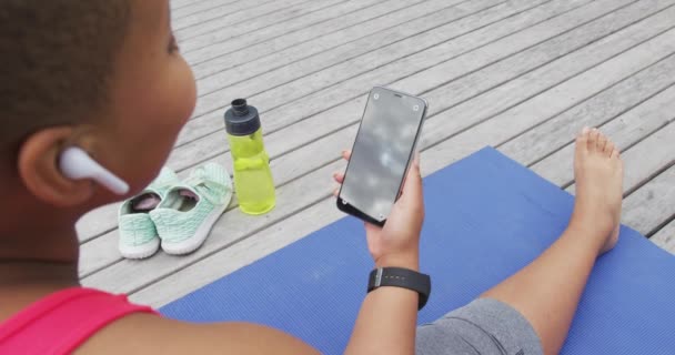 Szczęśliwa Afroamerykanka Ćwicząca Jogę Siedząca Pomocą Smartfona Pokładzie Ogrodzie Zdrowy — Wideo stockowe