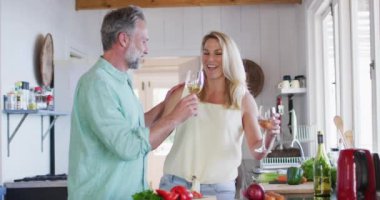 Kafkasyalı mutlu, olgun bir çift birlikte yemek pişiriyor ve mutfakta şarap içiyor. Evde boş vakitlerin tadını çıkarıyorum..