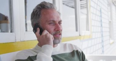 Kafkasyalı olgun bir adam terasta oturup akıllı telefon kullanıyor. Sahildeki evdeki boş vakitlerin tadını çıkarıyorum..