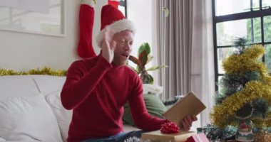 Mutlu albino Afrikalı Amerikalı adam Noel Baba şapkası takıyor ve Noel 'de video görüşmesi yapıyor. Noel, şenlik ve iletişim teknolojisi.