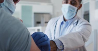 Yüz maskesi takan melez erkek doktor, erkek hastaya aşı yapıyor. Coronavirus covid 19 salgını sırasında hijyen, sağlık ve koruma.