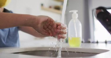 Kafkasyalı bir çocuğun mutfak lavabosunda durup ağır çekimde musluğun altında ellerini yıkaması. Kovid 19 koronavirüs karantinası sırasında sosyal uzaklık ve hijyen..