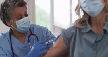 Kıdemli Afro-Amerikan kadın doktor kadın hasta aşılıyor. İkisi de yüz maskesi takıyor. Koronavirüs covid 19 salgını sırasında sağlık hizmetleri hijyen koruması.