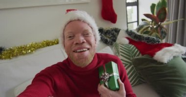 Mutlu albino Afrikalı Amerikalı adam Noel Baba şapkası takıyor ve Noel 'de video görüşmesi yapıyor. Noel, şenlik ve iletişim teknolojisi.