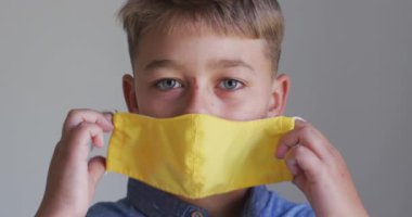 Beyaz bir çocuğun yakın plan portresi. Sarı bir maske takıyor, kameraya bakıyor. Kovid 19 koronavirüs karantinası sırasında sosyal uzaklık ve hijyen..