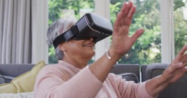 VR kulaklık takıp evde eğlenen son sınıf öğrencisi mutlu bir kadın. emeklilik hayatı teknolojiyle evde dinleniyor..