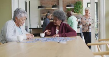 Bir grup mutlu kıdemli arkadaş kahve içip evde yapboz yapıyorlar. Evde arkadaşlarla sosyalleşmek..