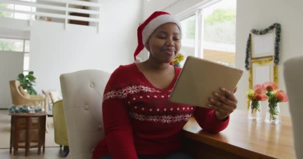 サンタ帽子の幸せなアフリカ系アメリカ人とサイズの女性は クリスマスにタブレットを使用してビデオ通話を行います クリスマス冬伝統お祝い家で — ストック動画