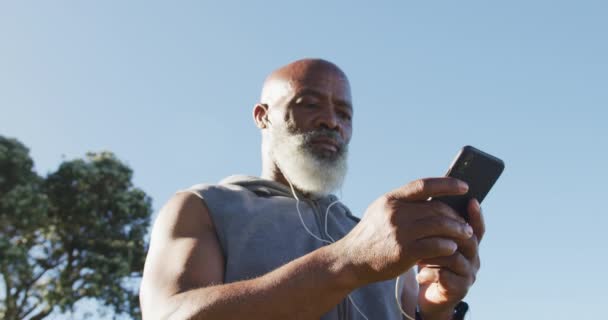 Hombre Afroamericano Mayor Haciendo Ejercicio Usando Teléfono Inteligente Colocando Auriculares — Vídeo de stock