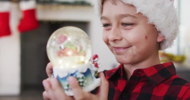 Blanke Jongen Viert Kerst Kijkt Naar Een Sneeuwbol Speelgoed Glimlacht — Stockvideo