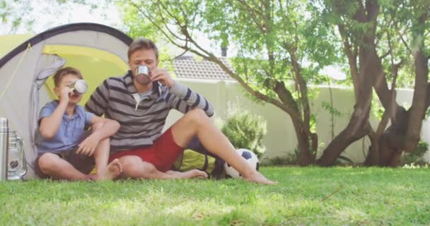 Hombre Caucásico Sentado Junto Una Tienda Con Hijo Jardín Bebiendo — Vídeos de Stock