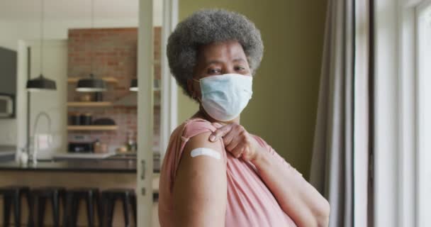 幸せなアフリカ系アメリカ人のシニア女性の顔のマスクを腕の上に石膏を示すワクチン接種後 感染症の流行期における高齢者の健康と生活 — ストック動画