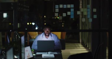 Masada dizüstü bilgisayar kullanan yorgun Afro-Amerikan iş adamının videosu. Geceleri ofiste yalnız çalışıyor. İş, iletişim, kapsayıcılık ve dijital olarak oluşturulan esnek çalışma konsepti.