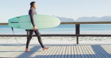 Dalgıç kıyafetli beyaz bir adamın güneşli gezinti güvertesinde sörf tahtası taşıdığı video. Özgürlük, spor, hobiler ve dijital olarak üretilen sağlıklı aktif yaşam tarzı konsepti.