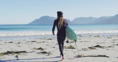 Güneşli sahilde sörf tahtası taşıyan, kafkasyalı, dalgıç kıyafetli bir adamın dikiz görüntüsü. Özgürlük, spor, hobiler ve dijital olarak üretilen sağlıklı aktif yaşam tarzı konsepti.