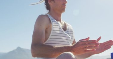 Rastalı beyaz adamın videosu. Yoga meditasyonu yapıyor. Güneşin altında oturuyor. Özgürlük, refah ve sağlıklı yaşam tarzı konsepti dijital olarak oluşturulmuş video.