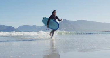Dalgıç kıyafetli beyaz bir adamın denizden güneşli plajlara sörf tahtası taşıdığı bir video. Özgürlük, spor, hobiler ve dijital olarak üretilen sağlıklı aktif yaşam tarzı konsepti.