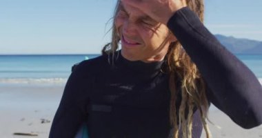 Güneşli sahilde dalgıç kıyafetiyle duran Kafkas erkek sörfçünün video portresi. Özgürlük, spor, hobiler ve dijital olarak üretilen sağlıklı aktif yaşam tarzı konsepti.