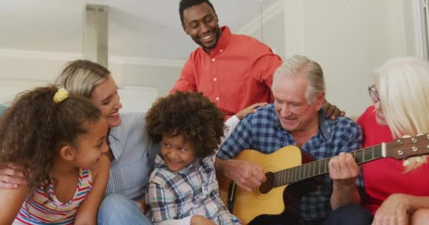 ソファに座っている多様な家族と ギターを弾いている祖父のビデオ 家族生活 家族と一緒に時間を過ごす — ストック動画