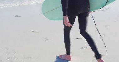 Dalgıç kıyafetli beyaz bir adamın güneşli sahilde sörf tahtası ile denize açılışının videosu. Özgürlük, spor, hobiler ve dijital olarak üretilen sağlıklı aktif yaşam tarzı konsepti.