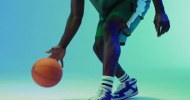Afrika kökenli Amerikalı erkek basketbolcunun mavi arka planda top sektirme videosu. Spor ve rekabet konsepti.