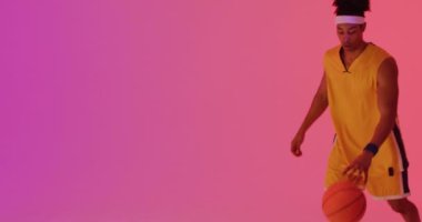 Çift ırklı erkek basketbolcunun turuncu üzerine pembe arka plana top attığı bir video. Spor ve rekabet konsepti.