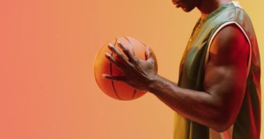 Afrikalı Amerikalı erkek basketbolcunun turuncu arka planda dönen topu videosu. Spor ve rekabet konsepti.