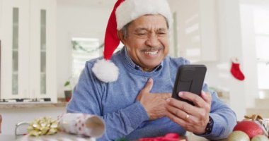 Noel Baba şapkalı son sınıf melezinin akıllı telefondan yılbaşı videosu çekerken videosu. Noel, gelenek, küresel iletişim, kapsayıcılık ve kıdemli yaşam tarzı konsepti.