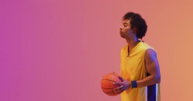 Çift ırklı erkek basketbolcunun turuncu üzerine pembe arka plana top attığı bir video. Spor ve rekabet konsepti.