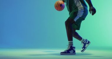 Afrika asıllı Amerikalı erkek basketbolcunun mavi arka planda zıplayan topu videosu. Spor ve rekabet konsepti.