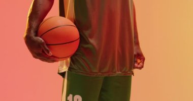 Turuncu arka planda topu tutan Afrikalı Amerikalı erkek basketbolcunun orta bölüm videosu. Spor ve rekabet konsepti.