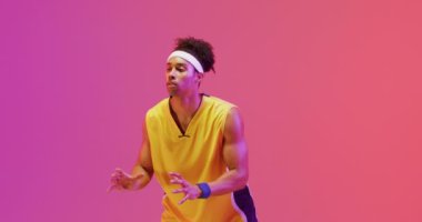 Çift ırklı erkek basketbolcunun turuncu ve pembe arka planda top yakalama videosu. Spor ve rekabet konsepti.