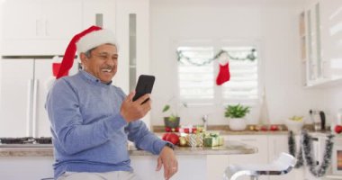 Noel Baba şapkalı son sınıf melez bir adamın akıllı telefondan yılbaşı görüntüsü alıp el salladığı bir video. Noel, gelenek, küresel iletişim, kapsayıcılık ve kıdemli yaşam tarzı konsepti.