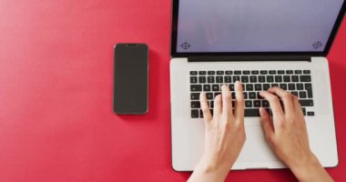 Eller kırmızı masada bilgisayarı ve akıllı telefonu kullanıyor. İş, iletişim ve uzaktan çalışma konsepti dijital olarak oluşturulmuş video.