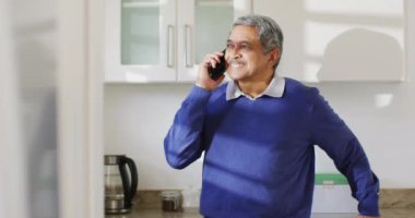 Mutfakta akıllı telefonla konuşan, gülümseyen üst düzey melez bir adamın videosu. Emeklilik, iletişim, kapsayıcılık ve kıdemli yaşam tarzı konsepti.