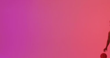 Çift ırklı erkek basketbolcunun turuncu üzerine pembe arka plana top attığı bir video. Spor ve rekabet konsepti.