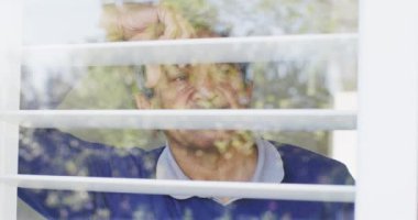Düşünceli üst düzey melez bir adamın pencereden dışarı bakıp eğildiği bir video. Emeklilik, sağlık, kapsayıcılık ve yaşlılar yaşam tarzı konsepti.
