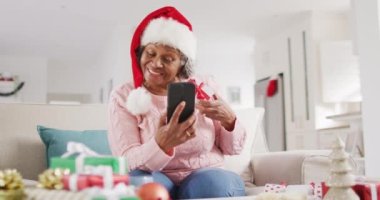 Mutlu son sınıf Afro-Amerikan kadını Noel 'de akıllı telefon kullanarak video araması yapıyor. Emeklilik, evde vakit geçirme ve Noel konsepti.