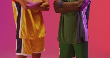 Pembe arka planda kolları çapraz olan iki farklı erkek basketbolcunun portresi. Spor ve rekabet konsepti.