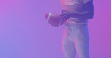 Afro-Amerikan Amerikan futbolcusunun orta bölüm videosu. Mor arka planda topu var. Amerikan futbolu, spor ve yarışma konsepti.