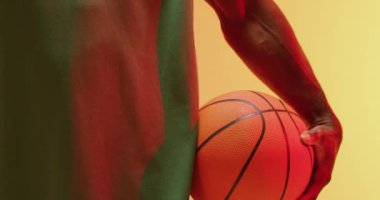 Turuncu arka planda topu tutan Afrikalı Amerikalı erkek basketbolcunun orta bölüm videosu. Spor ve rekabet konsepti.