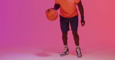 Afro-Amerikan erkek basketbolcunun pembe arka planda turuncu topa zıpladığı bir video. Spor ve rekabet konsepti.