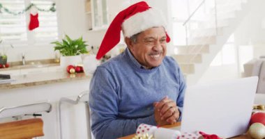 Noel Baba şapkalı mutlu, çift ırklı bir adamın Noel 'de dizüstü bilgisayarını açıp hediyesini tuttuğu bir video. Noel, gelenek, küresel iletişim, kapsayıcılık ve kıdemli yaşam tarzı konsepti.