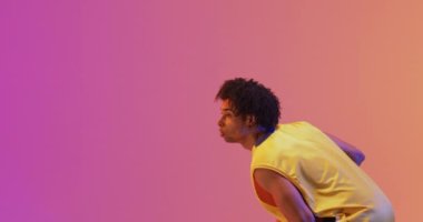 Çift ırklı erkek basketbolcunun turuncu üzerine pembe arka plana top attığı bir video. Spor ve rekabet konsepti.
