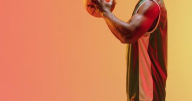 Turuncu arka planda topu tutan Afrikalı Amerikalı erkek basketbolcunun videosu. Spor ve rekabet konsepti.