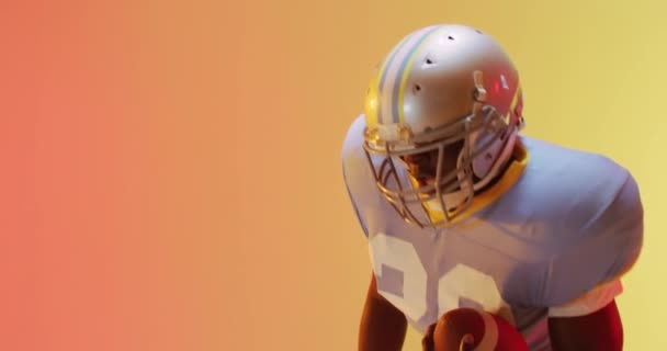 黄色からオレンジの背景にボールを持つアフリカ系アメリカ人アメリカ人サッカー選手のビデオ アメリカンフットボール スポーツ 競技のコンセプト — ストック動画