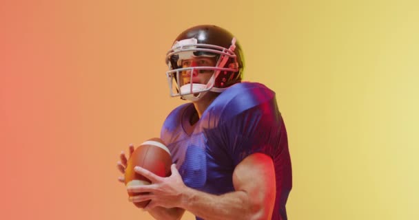 オレンジを背景にボールをヘルメットで白人アメリカ人サッカー選手のクローズアップのビデオ アメリカンフットボール スポーツ 競技のコンセプト — ストック動画