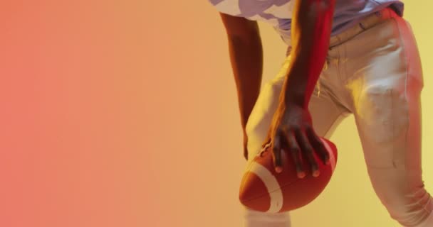 オレンジを背景にボールを持つアフリカ系アメリカ人アメリカ人サッカー選手のビデオ アメリカンフットボール スポーツ 競技のコンセプト — ストック動画