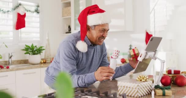 サンタの帽子で幸せなシニアの出産男のビデオクリスマスビデオ通話を作るタブレット吹いてキス クリスマス グローバルなコミュニケーション 包括性とシニアライフスタイルの概念 — ストック動画