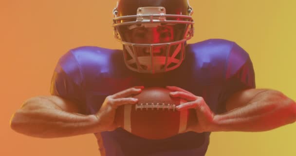 オレンジを背景にボールをヘルメットで白人アメリカ人サッカー選手のクローズアップのビデオ アメリカンフットボール スポーツ 競技のコンセプト — ストック動画